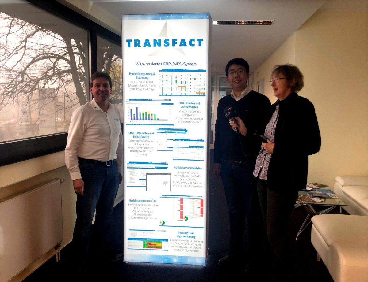 Anette Jaciuk vor Transfact Poster mit Heiko Martin und Yang Yang